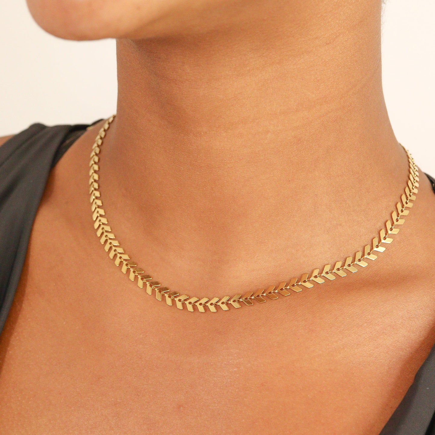 Elegant gold chevron herringbone chain necklace resting flat against skin, highlighting the smooth, reflective V-link pattern and timeless, statement-making design.
