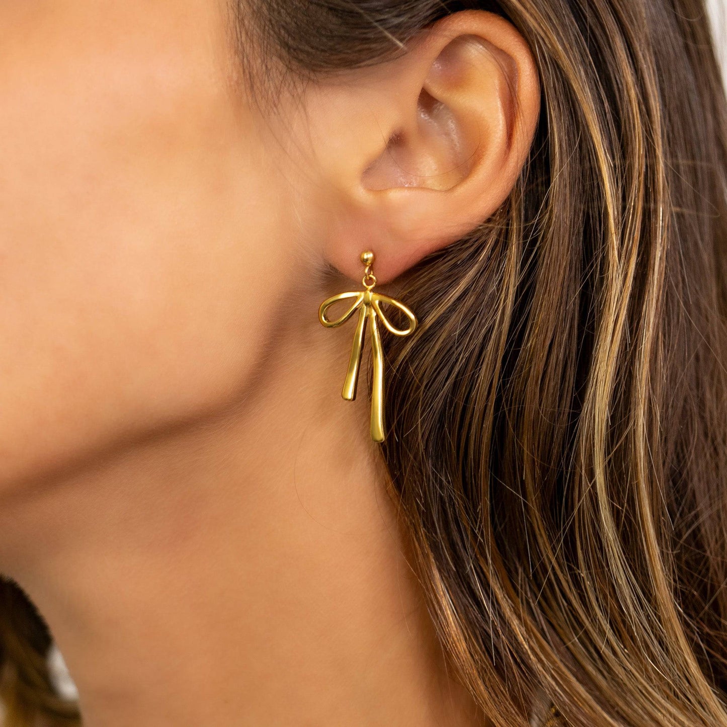 Close-up of a woman wearing a gold bow-shaped drop earring from Lauren Riley Jewelry. Waterproof, hypoallergenic, and perfect for everyday elegance.