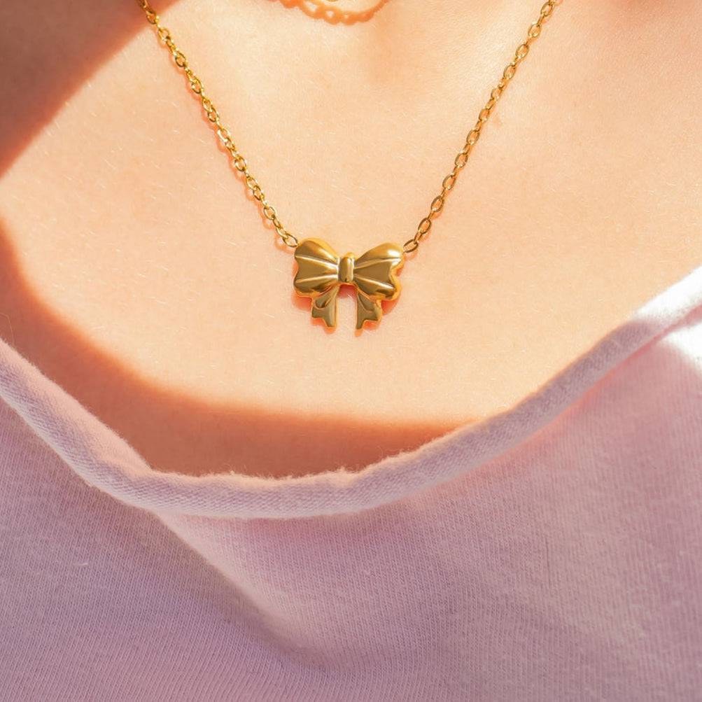 Close-up of gold bow necklace on model’s neck, waterproof and hypoallergenic by Lauren Riley Jewelry