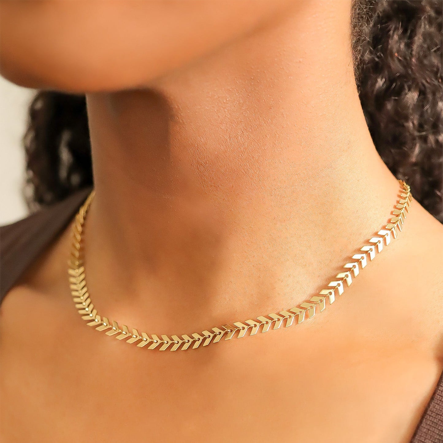 Close-up of a woman wearing a gold chevron herringbone chain necklace, showcasing the V-link design that lays flat against the neckline for a polished, elegant look.
