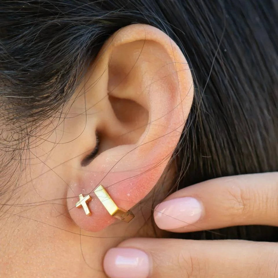Close-up of a woman wearing a gold cross stud and square huggie hoop earrings in a chic ear stack, styled by Lauren Riley Jewelry.