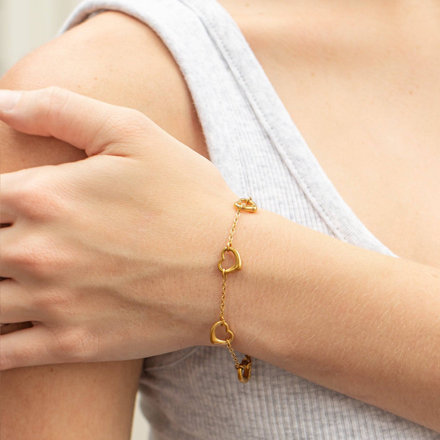 Gold heart bracelet on woman’s arm, dainty and waterproof minimalist jewelry, perfect for stacking and everyday wear.