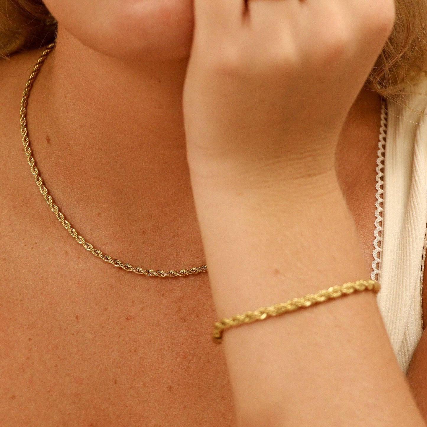 Close-up of woman wearing matching set of the gold rope chain necklace and bracelet.