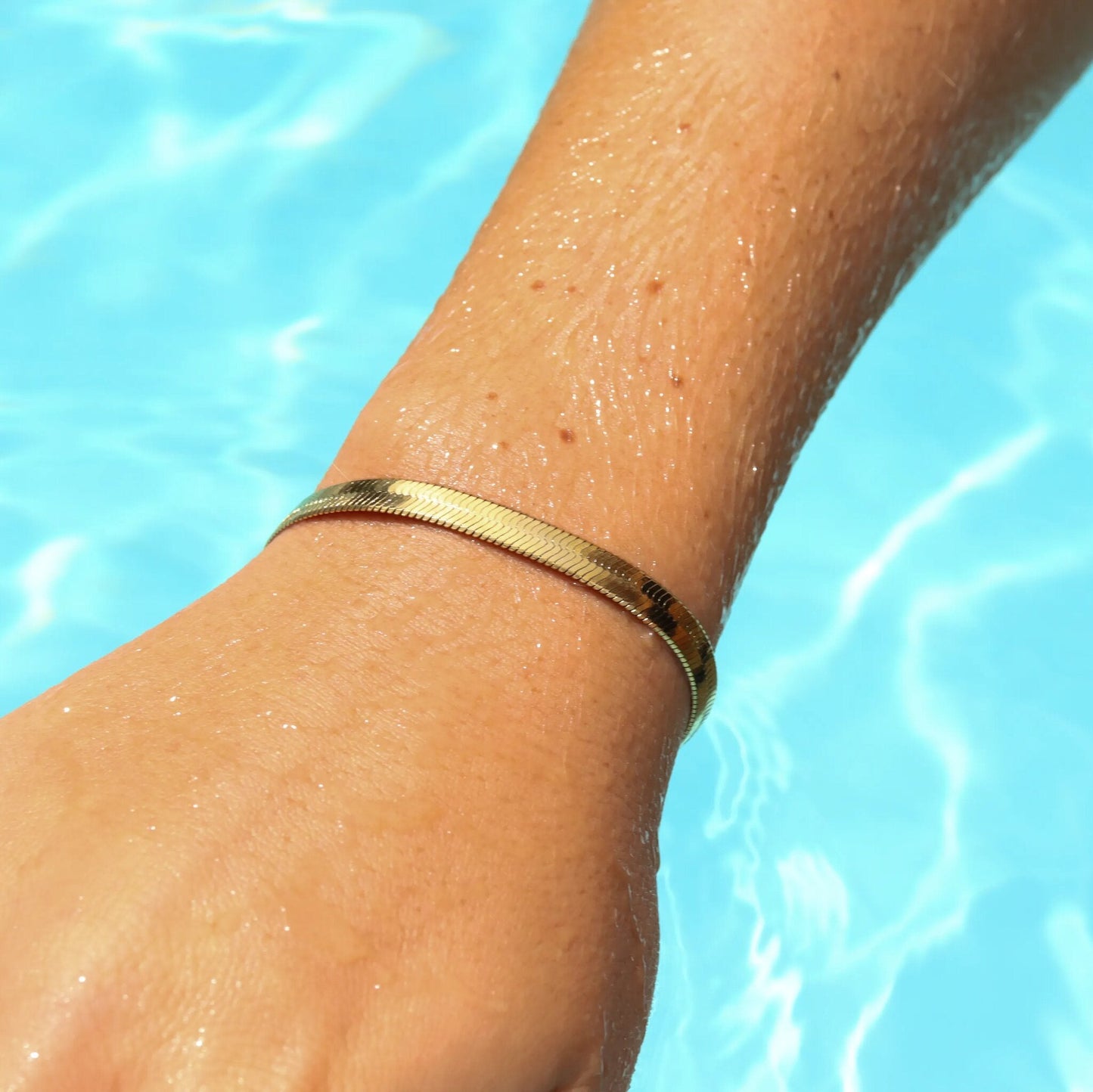 18k gold waterproof herringbone bracelet on wrist near pool – summer jewelry from Lauren Riley Jewelry.