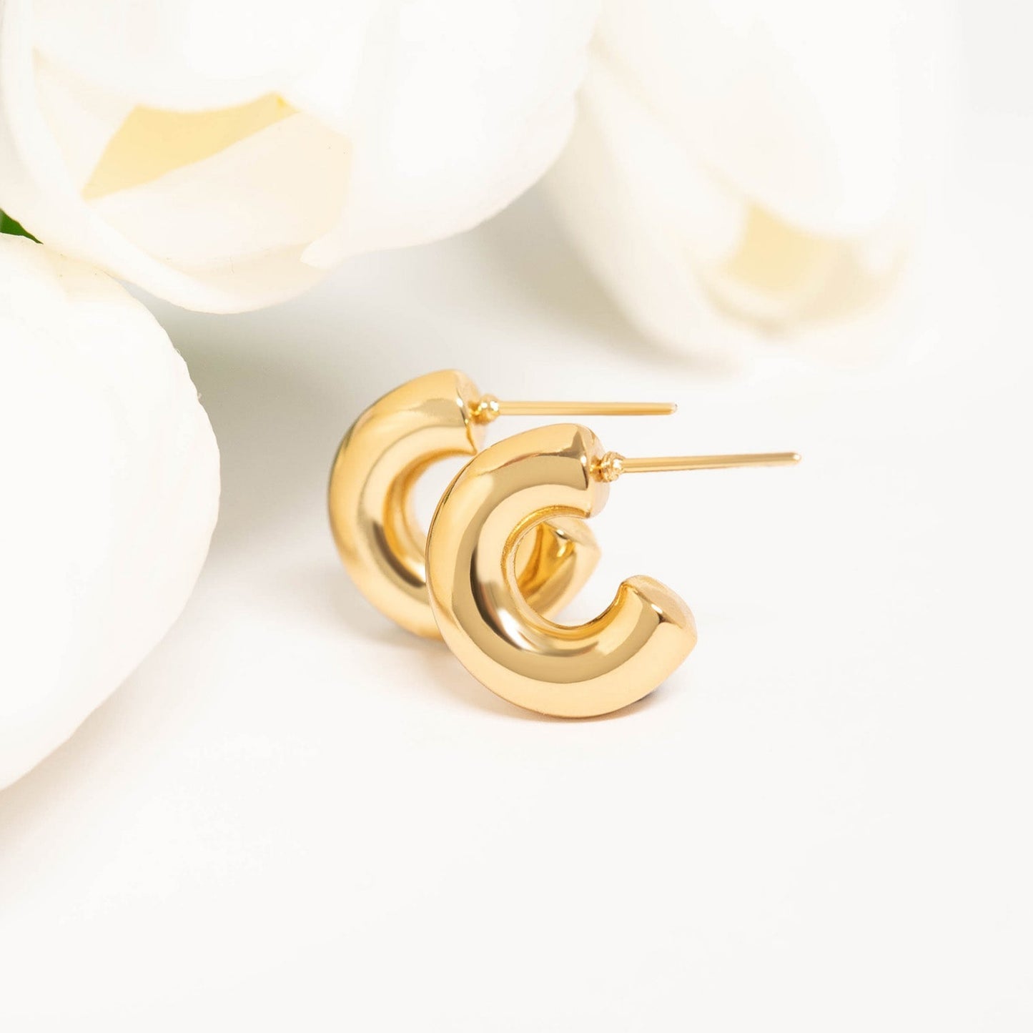 Gold waterproof hoop earrings displayed next to white tulips on a clean background, showcasing elegant and timeless design