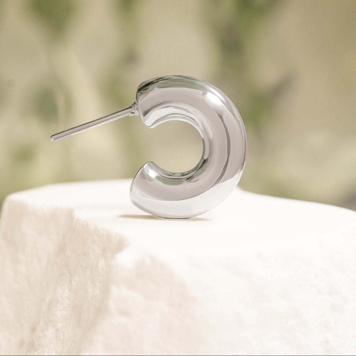 Polished silver waterproof hoop earring displayed on a stone pedestal with a soft natural background, highlighting minimalist luxury design