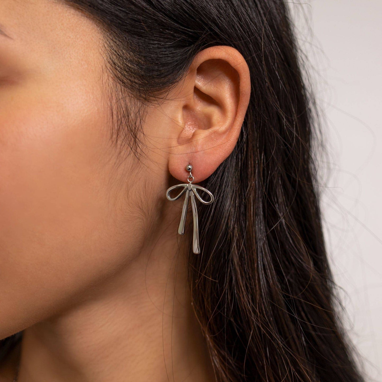 Side profile of a woman wearing silver bow drop earrings with a ribbon design. These hypoallergenic and waterproof earrings from Lauren Riley Jewelry are styled for everyday elegance and comfort.