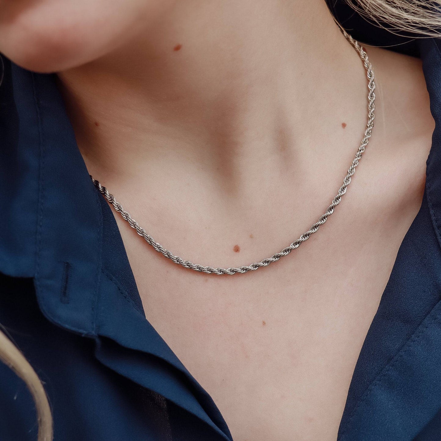 Close-up of a woman wearing a stainless teel silver rope chain necklace on her collarbone, styled with a navy blouse.