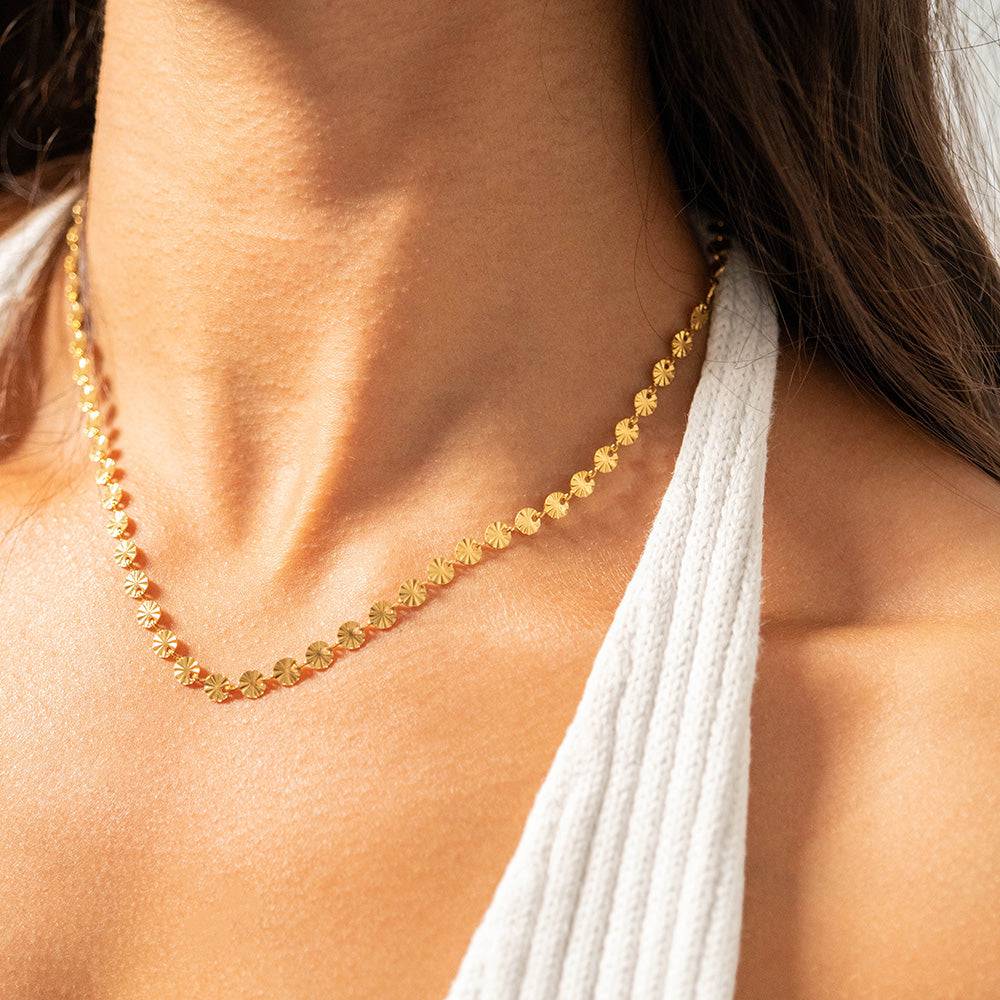 Close-up of gold sunburst disc chain necklace with 18k gold PVD finish, waterproof and tarnish-resistant, styled on model with white ribbed top