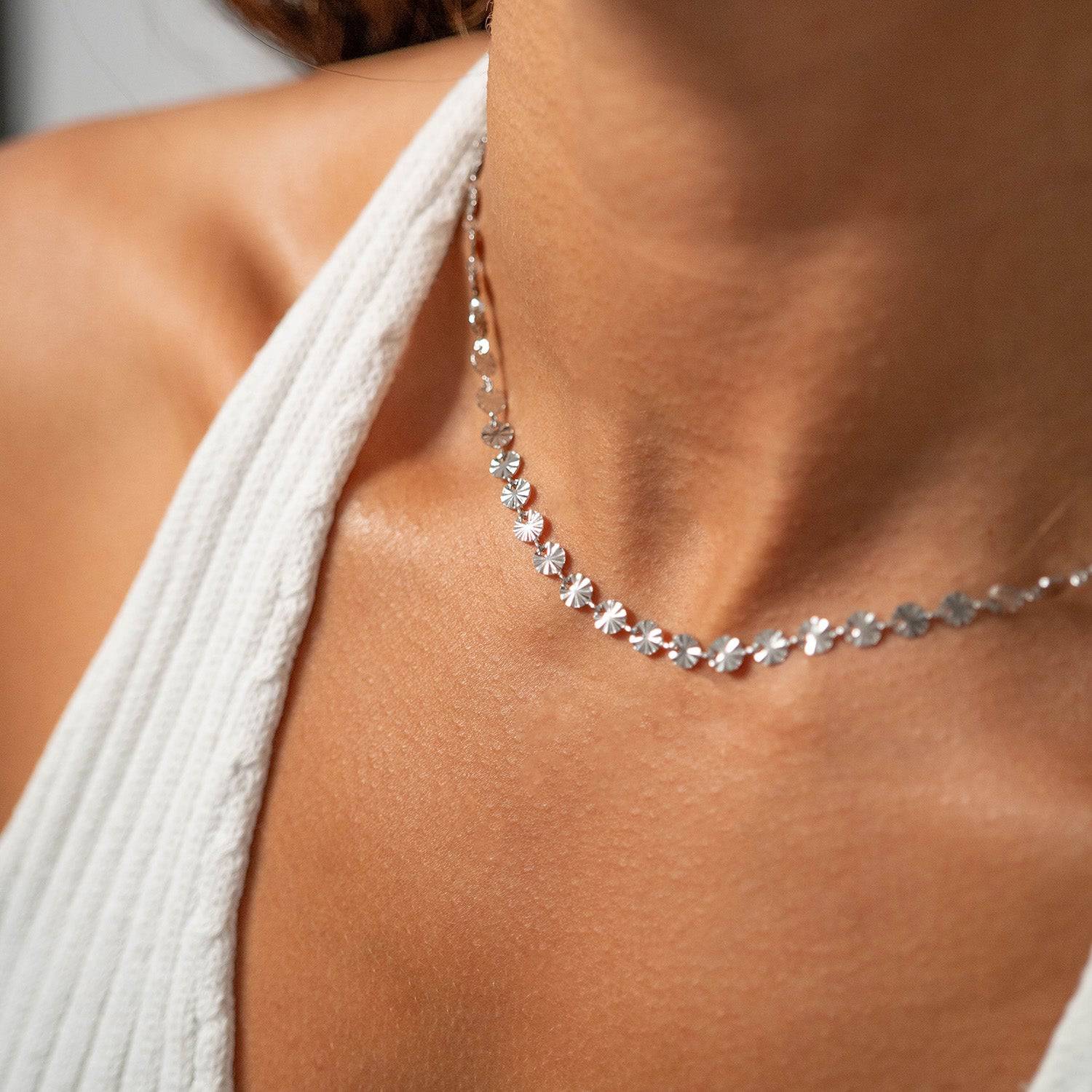 Close-up of silver sunburst disc chain necklace, waterproof and hypoallergenic, styled on model wearing white ribbed top