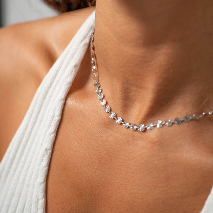 Close-up of silver sunburst disc chain necklace, waterproof and hypoallergenic, styled on model wearing white ribbed top
