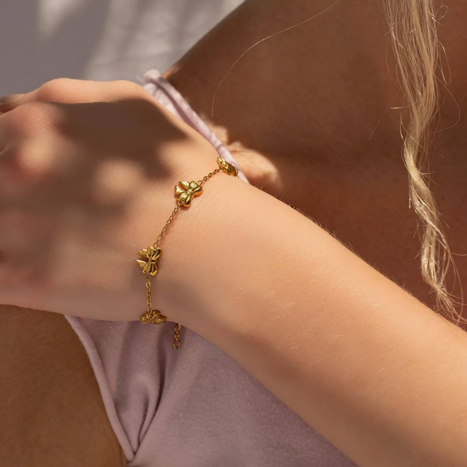 Close-up of gold bow bracelet stacked on wrist, made of waterproof and hypoallergenic 18k gold PVD stainless steel, perfect for everyday wear.