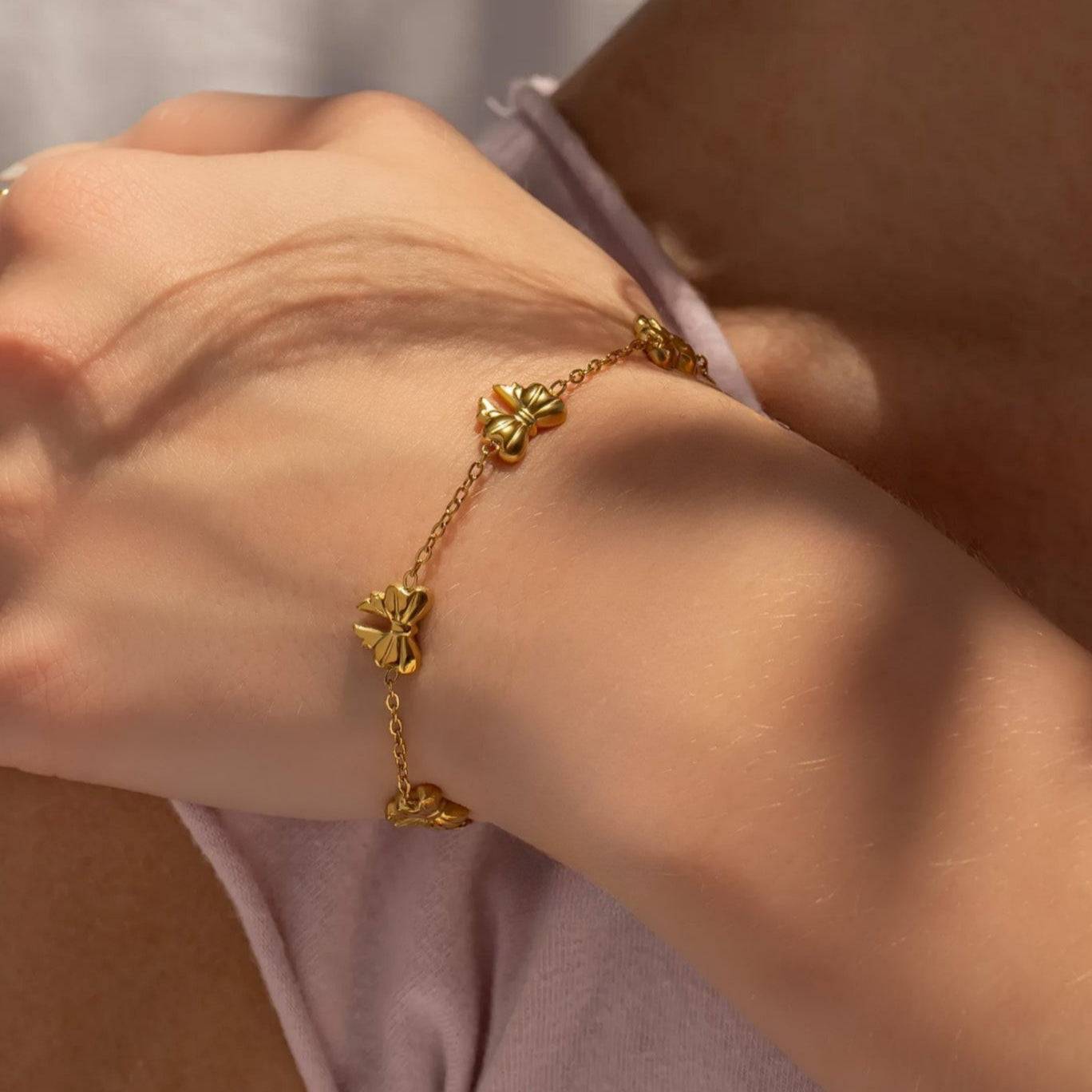 Gold bow charm bracelet on wrist, crafted from waterproof and hypoallergenic stainless steel with 18k gold PVD plating, ideal for everyday stacking.