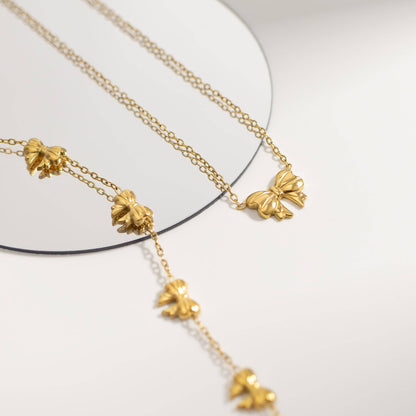 Gold bow necklace and bracelet set reflected in mirror, featuring dainty waterproof and tarnish-resistant chains for elegant everyday wear.

