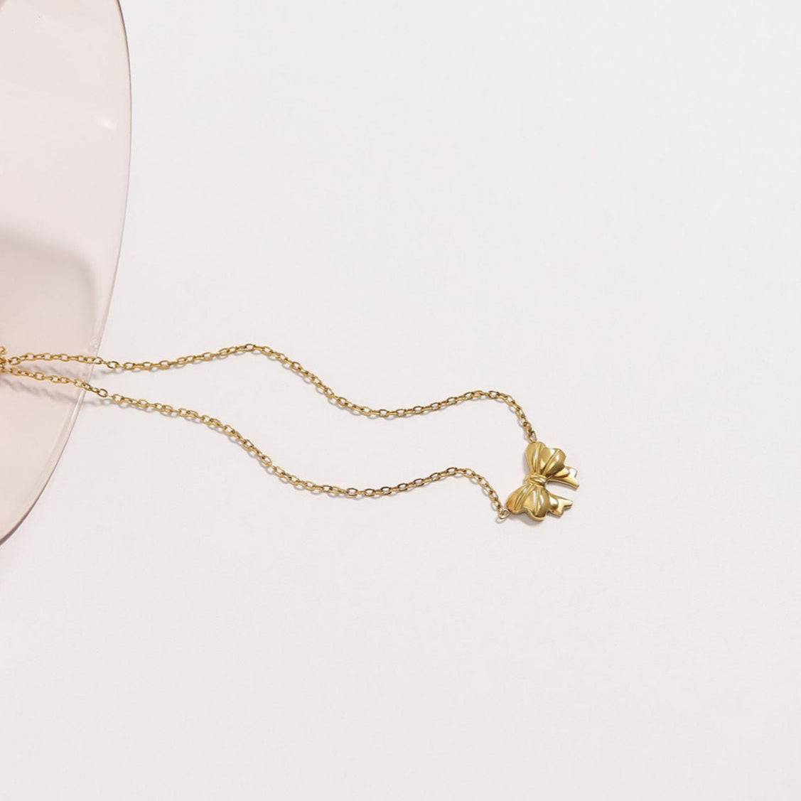 Gold bow pendant necklace styled on glass, delicate waterproof jewelry by Lauren Riley Jewelry