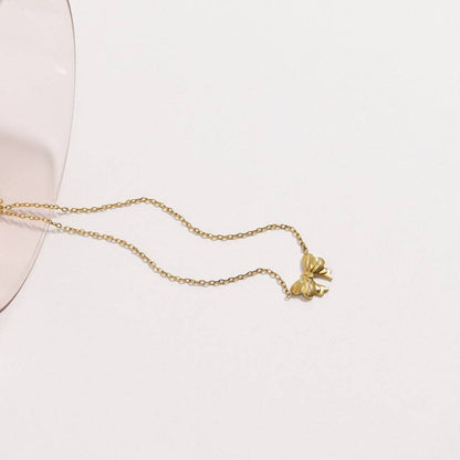Gold bow pendant necklace styled on glass, delicate waterproof jewelry by Lauren Riley Jewelry
