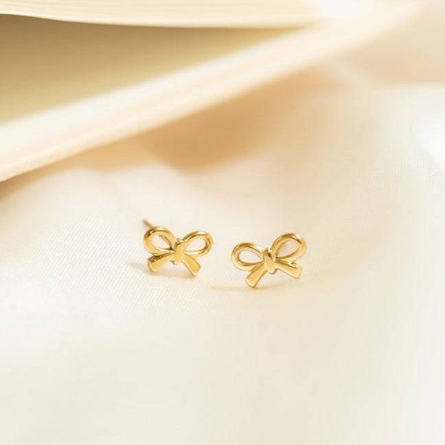 Elegant gold bow stud earrings resting on soft fabric, dainty hypoallergenic gift idea for her