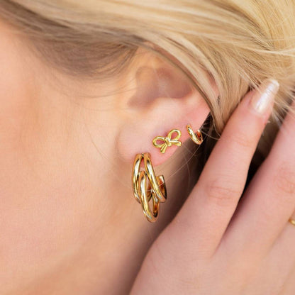 Dainty gold bow stud earrings paired with chunky gold hoops in a trendy stacked ear styling on blonde woman