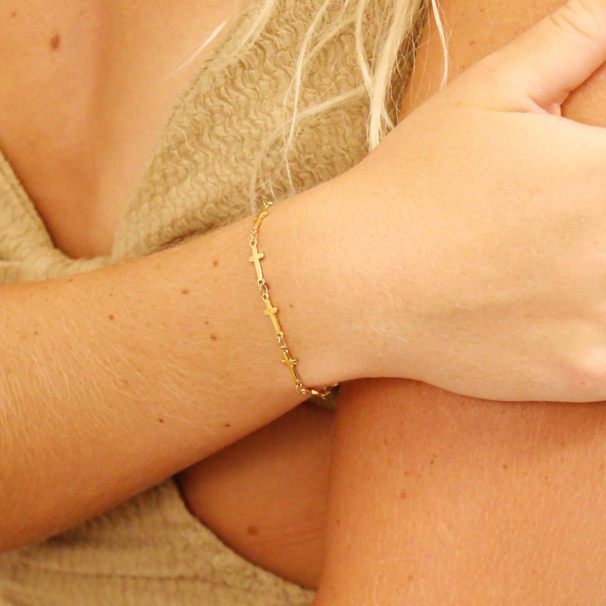 Dainty gold cross chain bracelet on wrist. Hypoallergenic, waterproof, and perfect for stacking or wearing solo. Stylish faith-inspired jewelry.