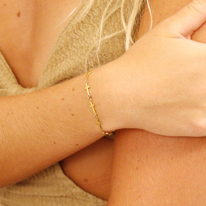 Dainty gold cross chain bracelet on wrist. Hypoallergenic, waterproof, and perfect for stacking or wearing solo. Stylish faith-inspired jewelry.