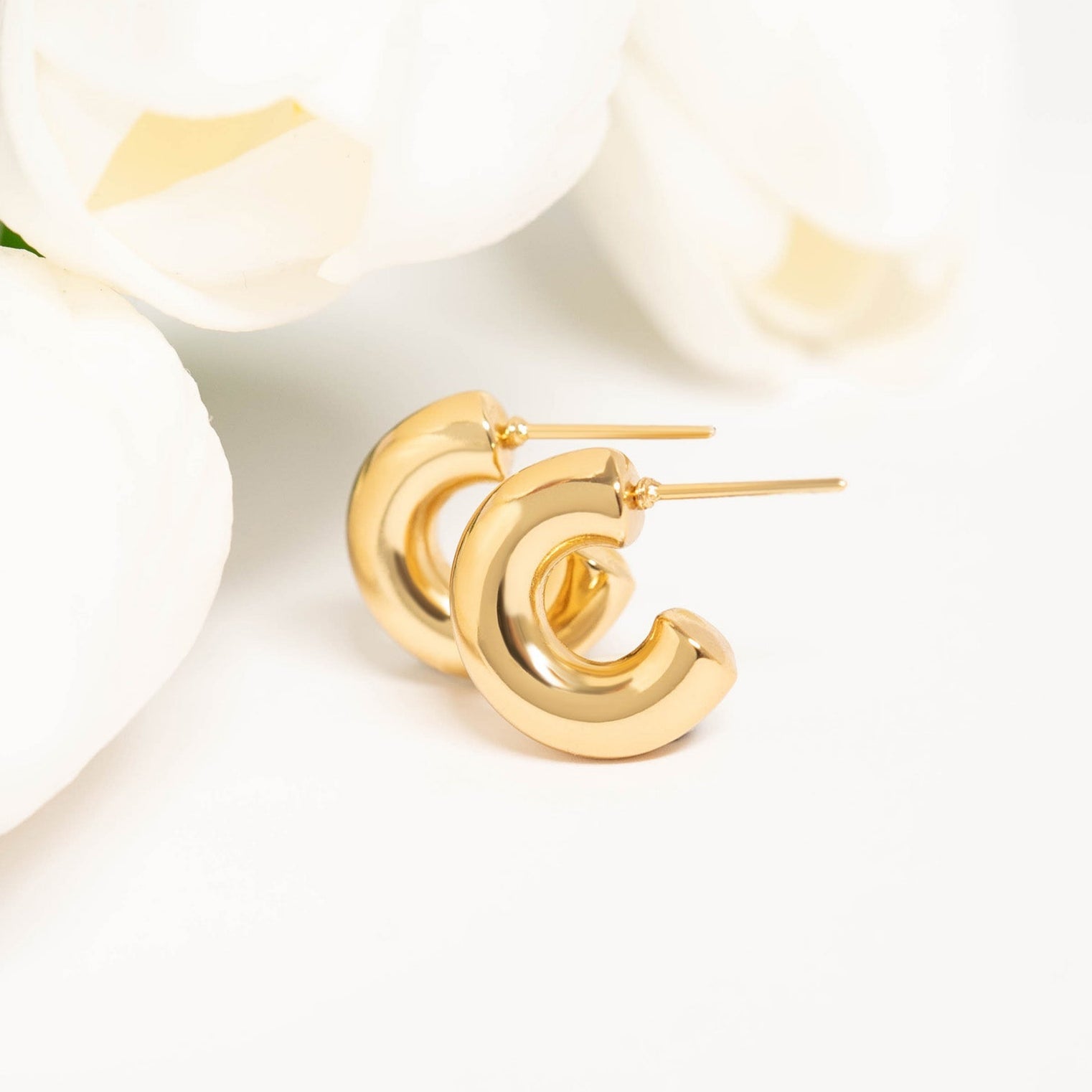 Gold waterproof hoop earrings displayed next to white tulips on a clean background, showcasing elegant and timeless design