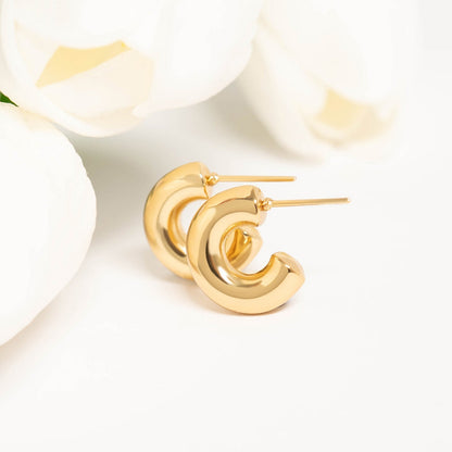 Gold waterproof hoop earrings displayed next to white tulips on a clean background, showcasing elegant and timeless design