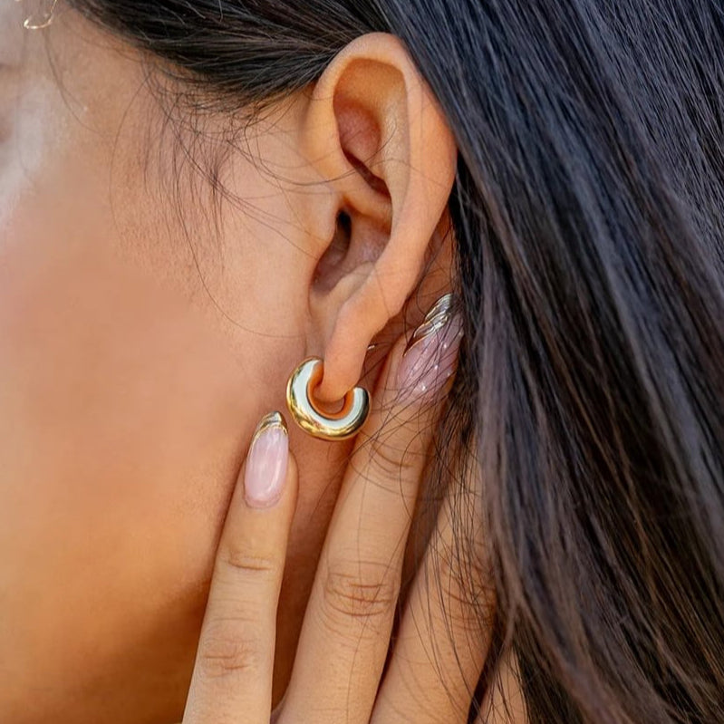Model wearing chunky gold waterproof hoop earrings with hand gently touching ear, perfect for casual summer styling