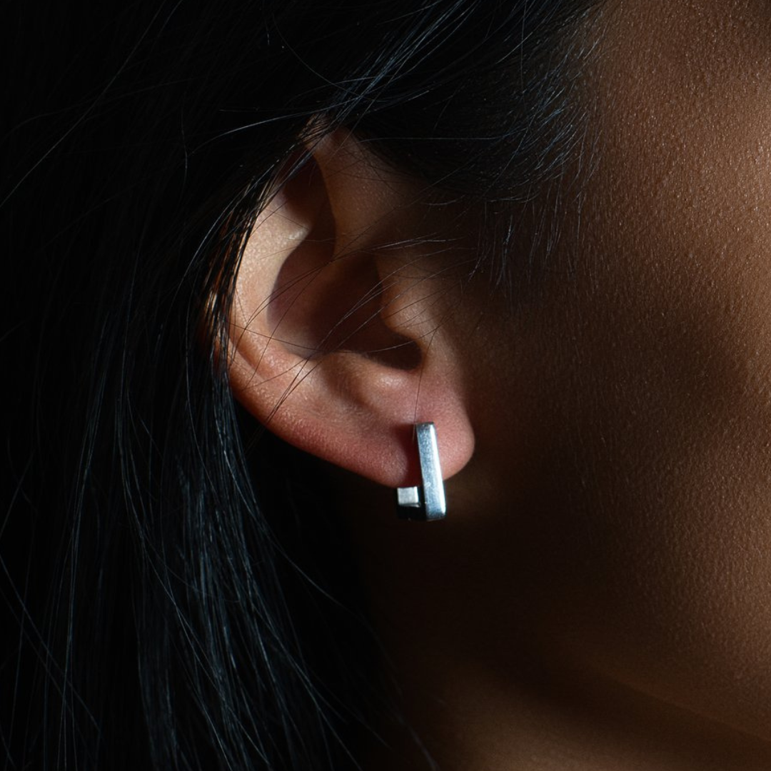 Close-up of a woman wearing a minimalist silver square hoop huggie earring, showcasing hypoallergenic, waterproof stainless-steel jewelry with a modern geometric design.