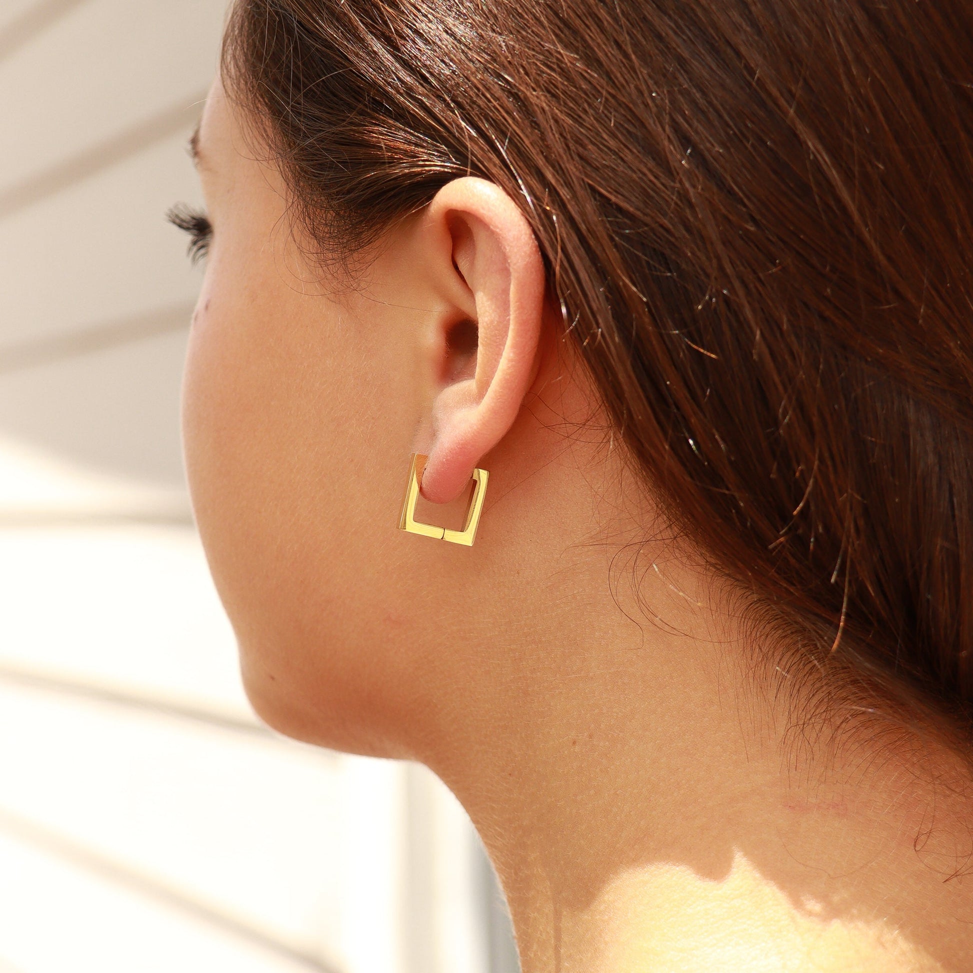 Close-up of woman wearing minimalist waterproof gold square hoop earrings — modern and lightweight everyday jewelry.