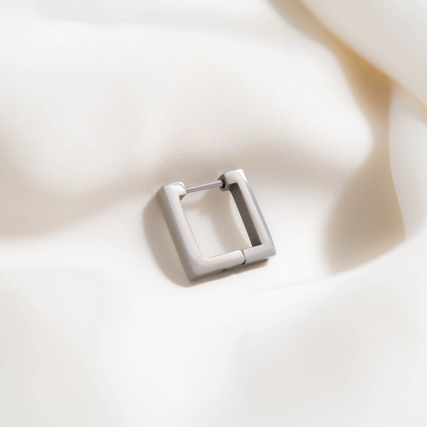 Single matte silver square hoop earring resting on soft ivory fabric — waterproof, hypoallergenic, and perfect for minimalist modern style.