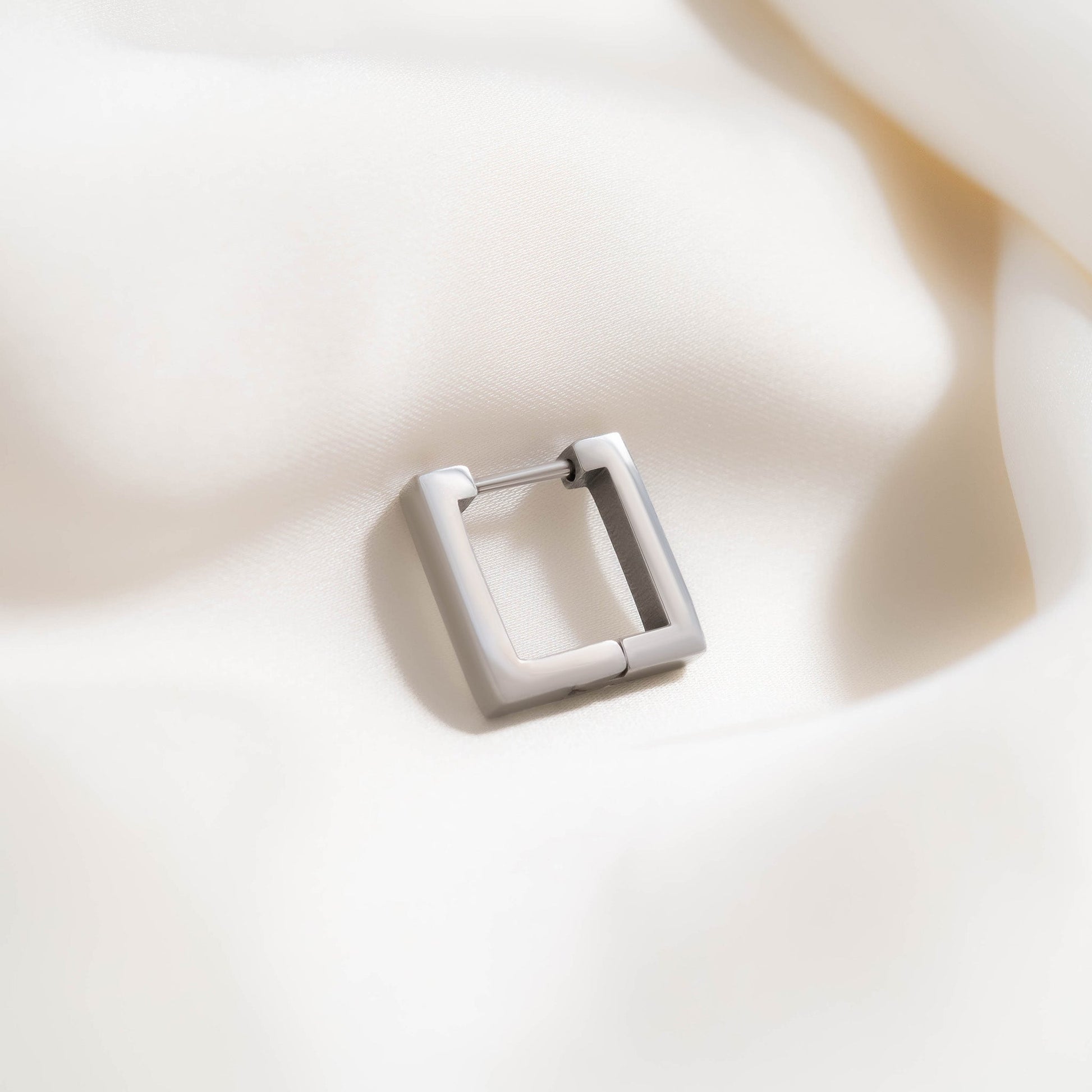 Single matte silver square hoop earring resting on soft ivory fabric — waterproof, hypoallergenic, and perfect for minimalist modern style.