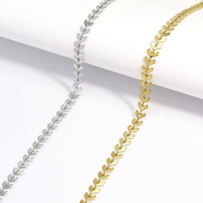 Flat lay display of gold and silver herringbone chain necklaces showcasing the sleek, reflective finish and elegant chevron design against a minimal white background.