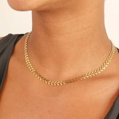 Elegant gold chevron herringbone chain necklace resting flat against skin, highlighting the smooth, reflective V-link pattern and timeless, statement-making design.