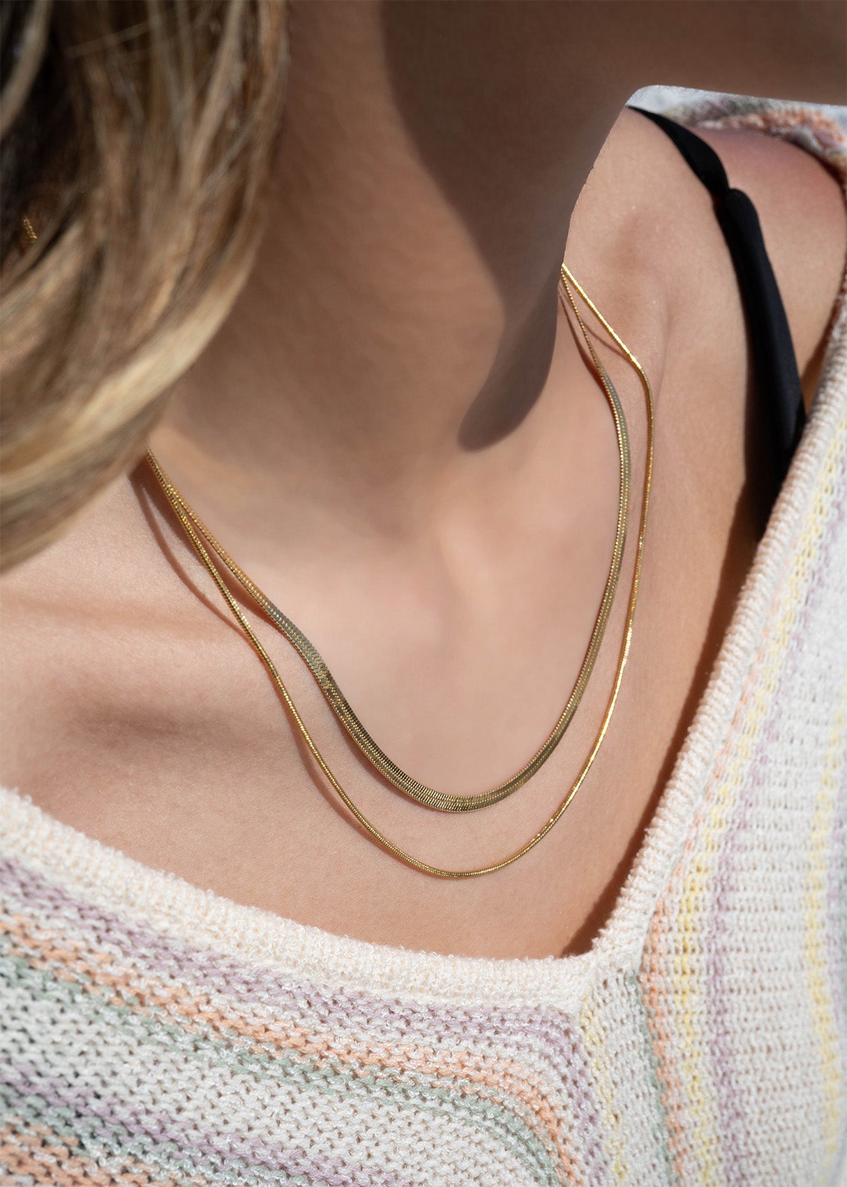 Close-up of gold layered herringbone necklace worn with a pastel knit sweater, perfect for everyday stacking