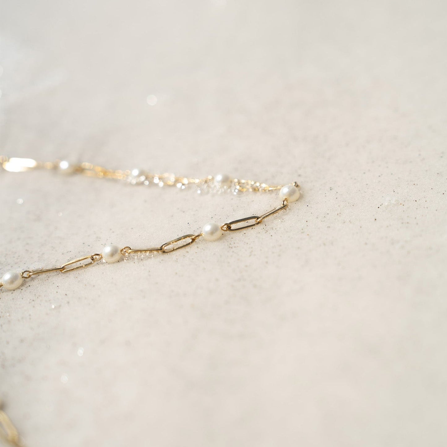 Delicate gold pearl paperclip necklace laying on sand – waterproof and hypoallergenic jewelry close-up