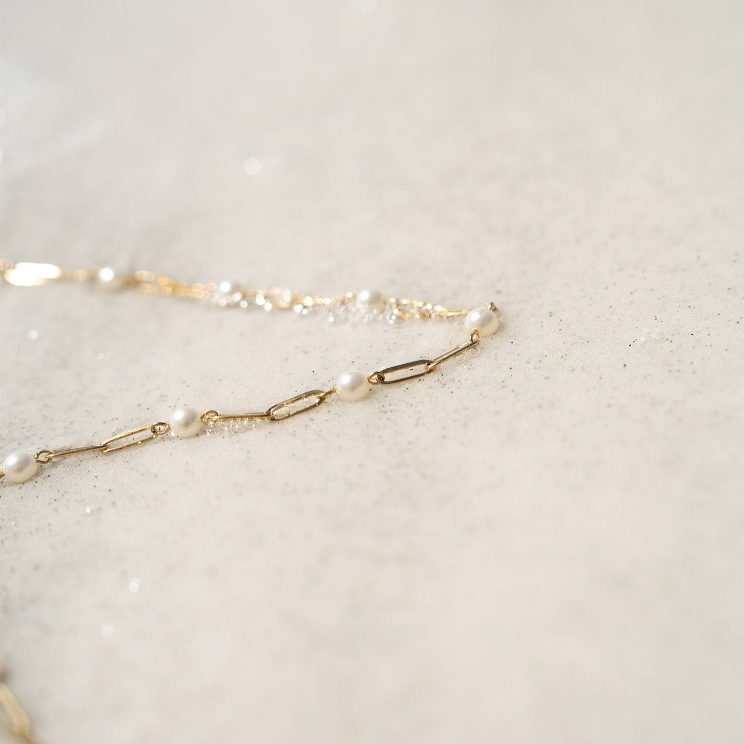 Delicate gold pearl paperclip necklace laying on sand – waterproof and hypoallergenic jewelry close-up
