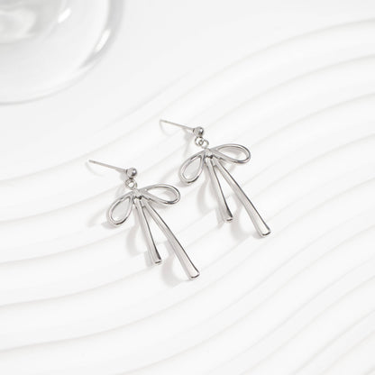 Pair of silver bow earrings displayed on a wavy white background. Dainty ribbon-inspired design that's hypoallergenic, tarnish-resistant, and perfect for everyday elegance from Lauren Riley Jewelry.