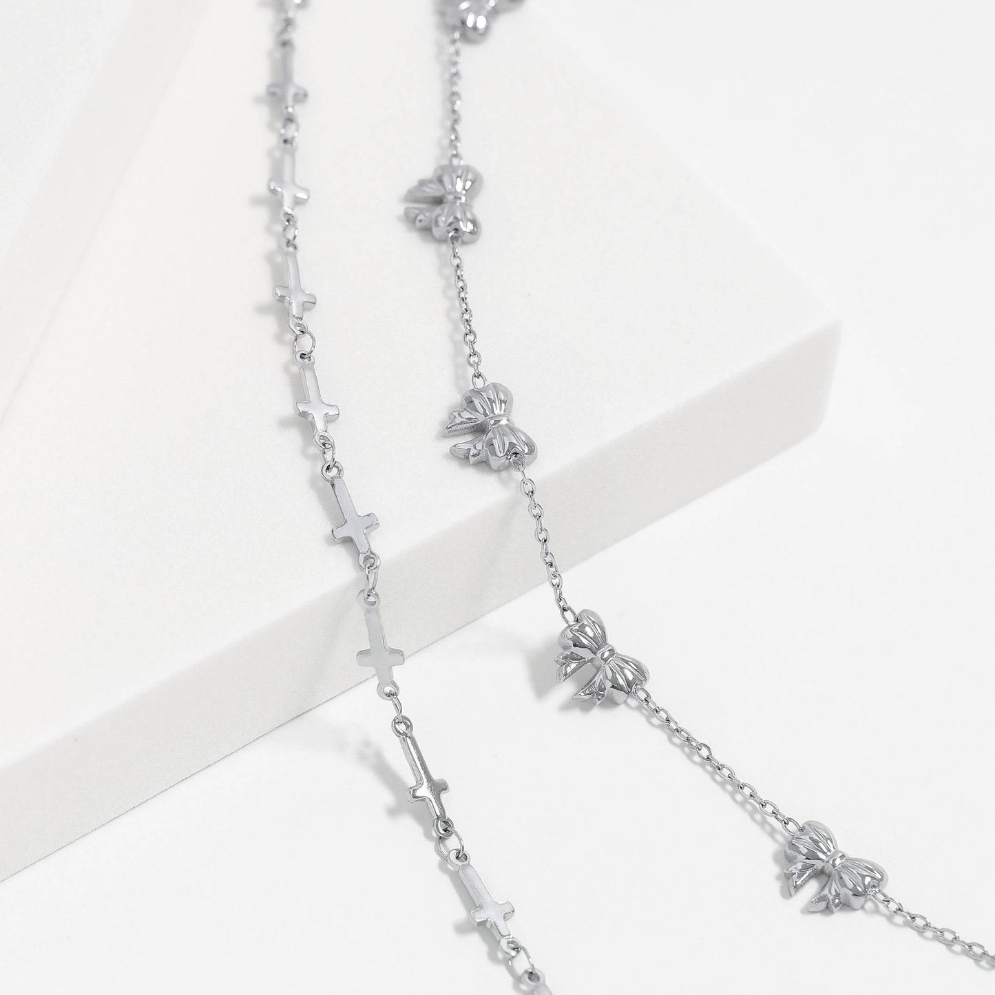 Silver cross and bow charm bracelets styled together on a white platform. Waterproof, hypoallergenic, and perfect for stacking or everyday minimalist wear.