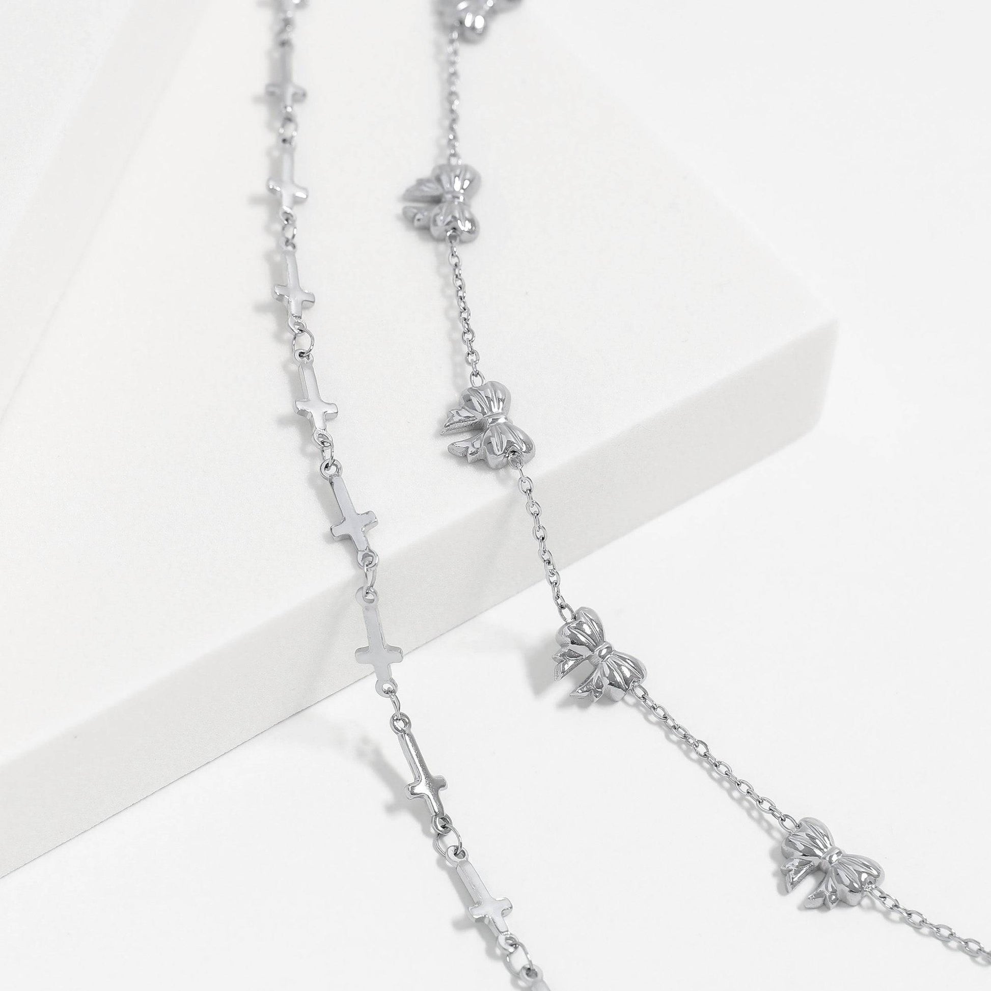 Silver cross and bow charm bracelets styled together on a white platform. Waterproof, hypoallergenic, and perfect for stacking or everyday minimalist wear.