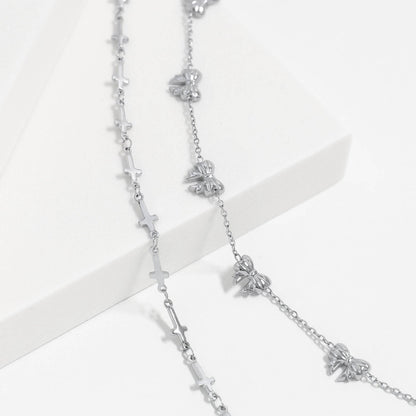 Silver cross and bow charm bracelets styled together on a white platform. Waterproof, hypoallergenic, and perfect for stacking or everyday minimalist wear.